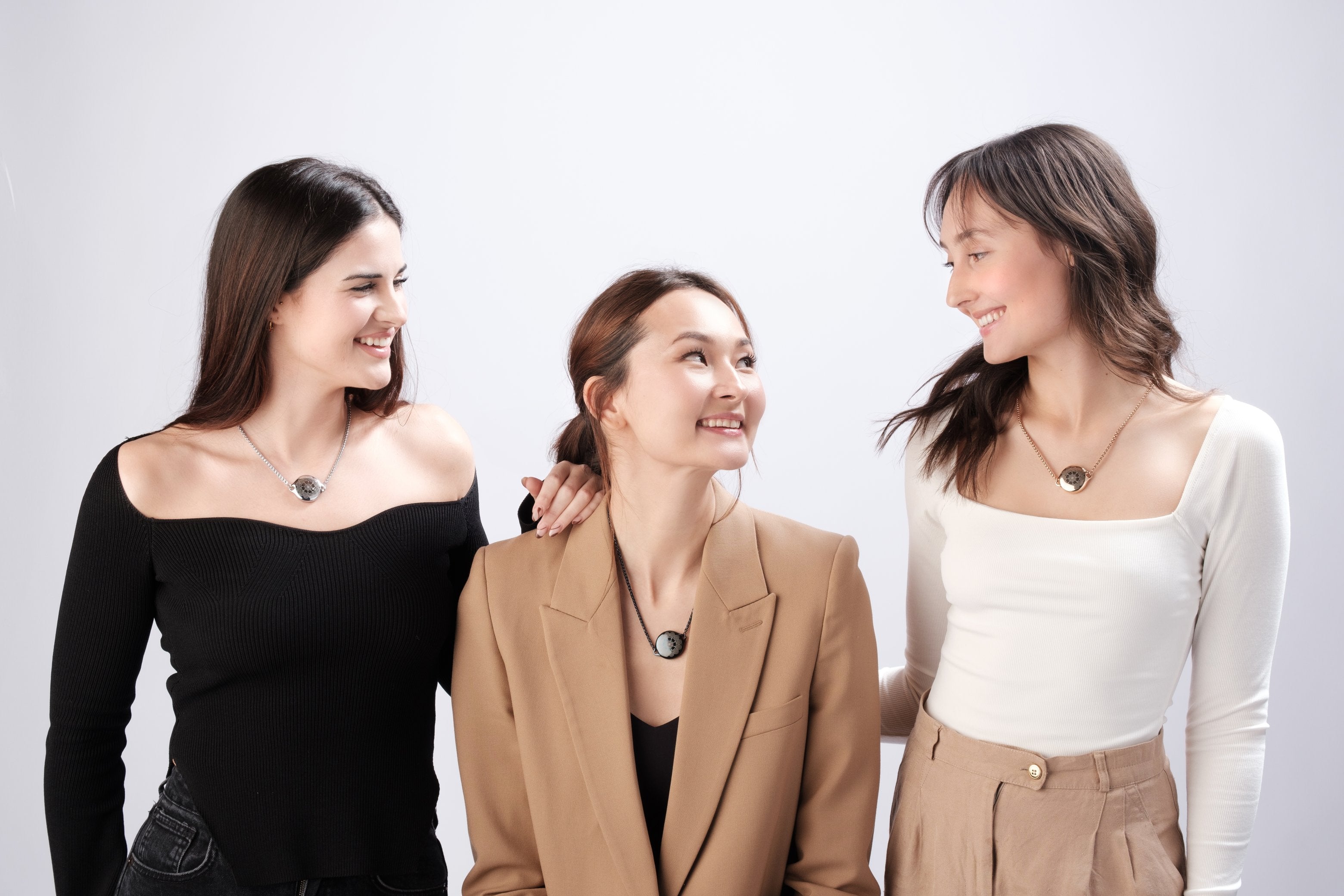 Three women friends wearing matching ResQ necklaces, smiling and embracing.